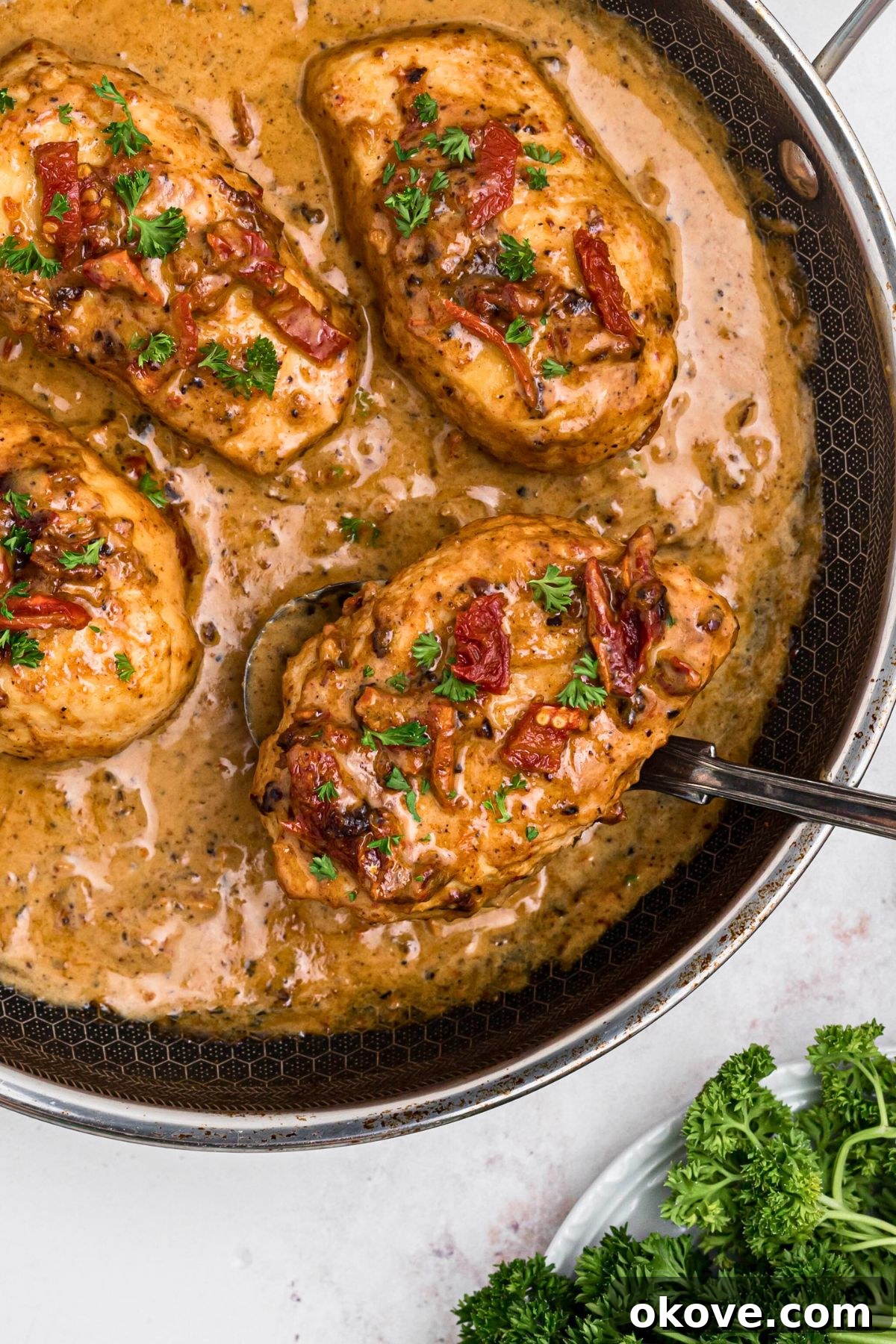 Say Yes Chicken 2 Creamy Marry Me Chicken in a large skillet, with a serving spoon lifting a tender piece of chicken from the rich sauce.