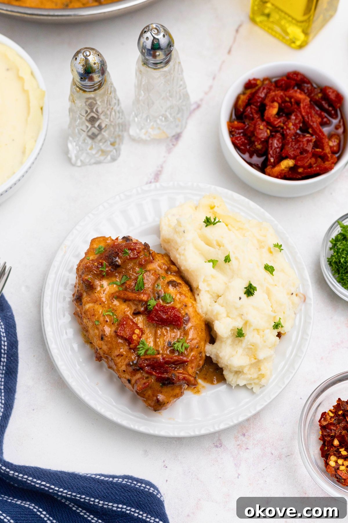 Say Yes Chicken 8 A perfectly golden, juicy Marry Me Chicken breast served on a white plate alongside a scoop of creamy mashed potatoes and fresh herbs.