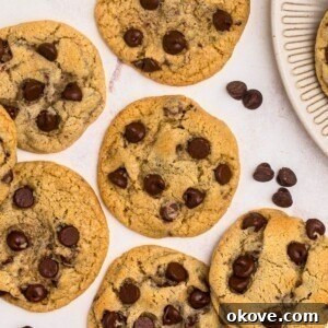 Golden brown chocolate chip cookies on a marble table with chocolate chips scattered around them.