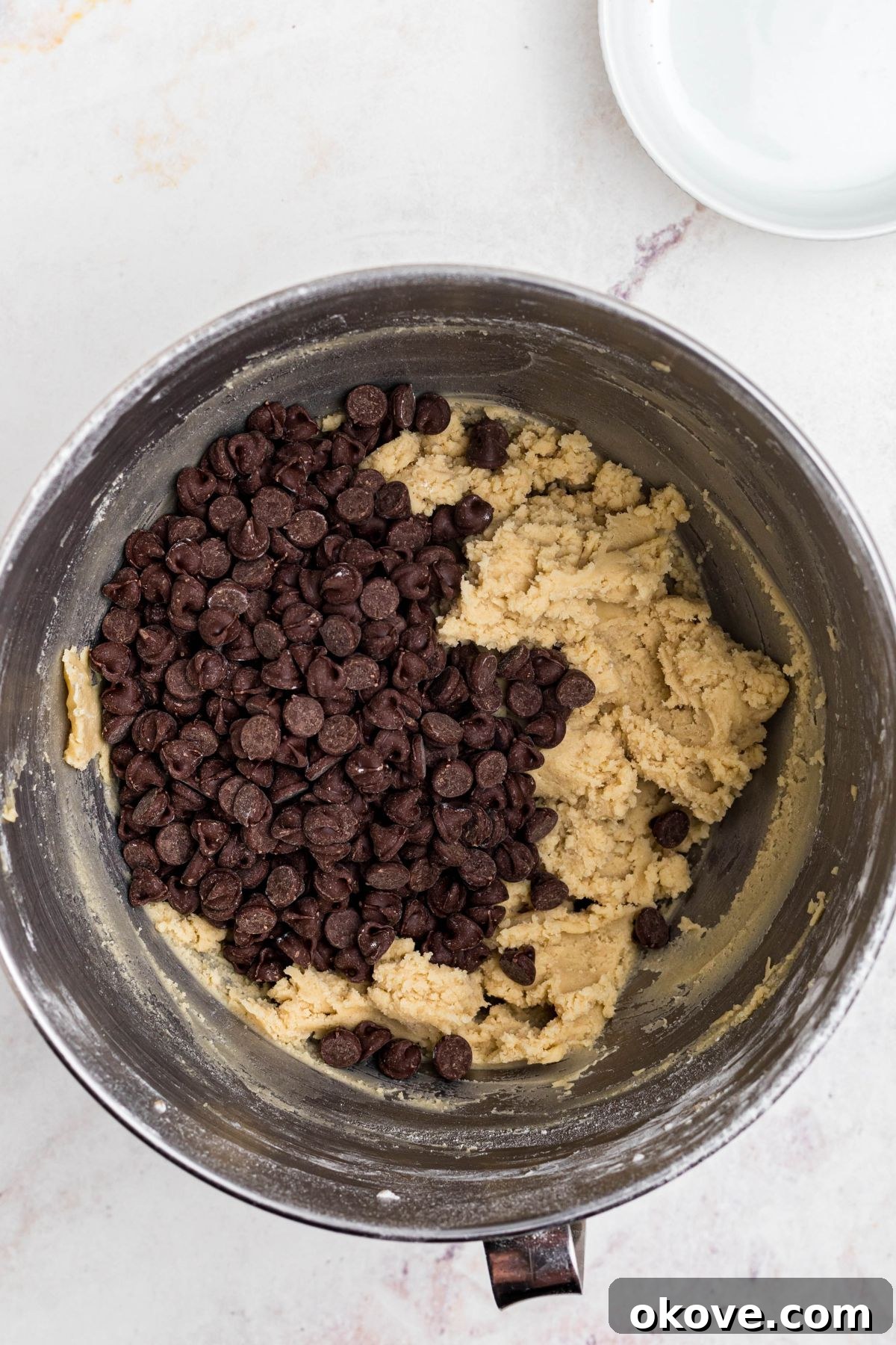 Warm Chocolate Chip Indulgence 5 Soft cookie dough in a mixing bowl with semi-sweet chocolate chips being added, ready to be incorporated.