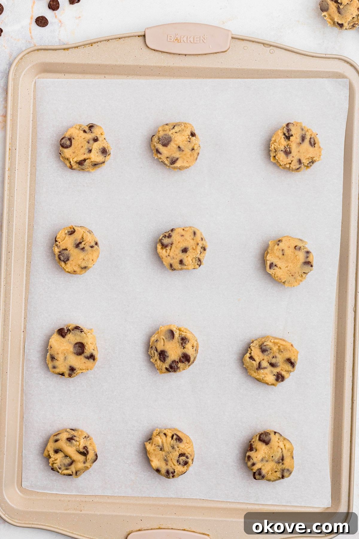 Warm Chocolate Chip Indulgence 6 Portions of chocolate chip cookie dough in small balls, neatly arranged on a baking sheet lined with parchment paper.