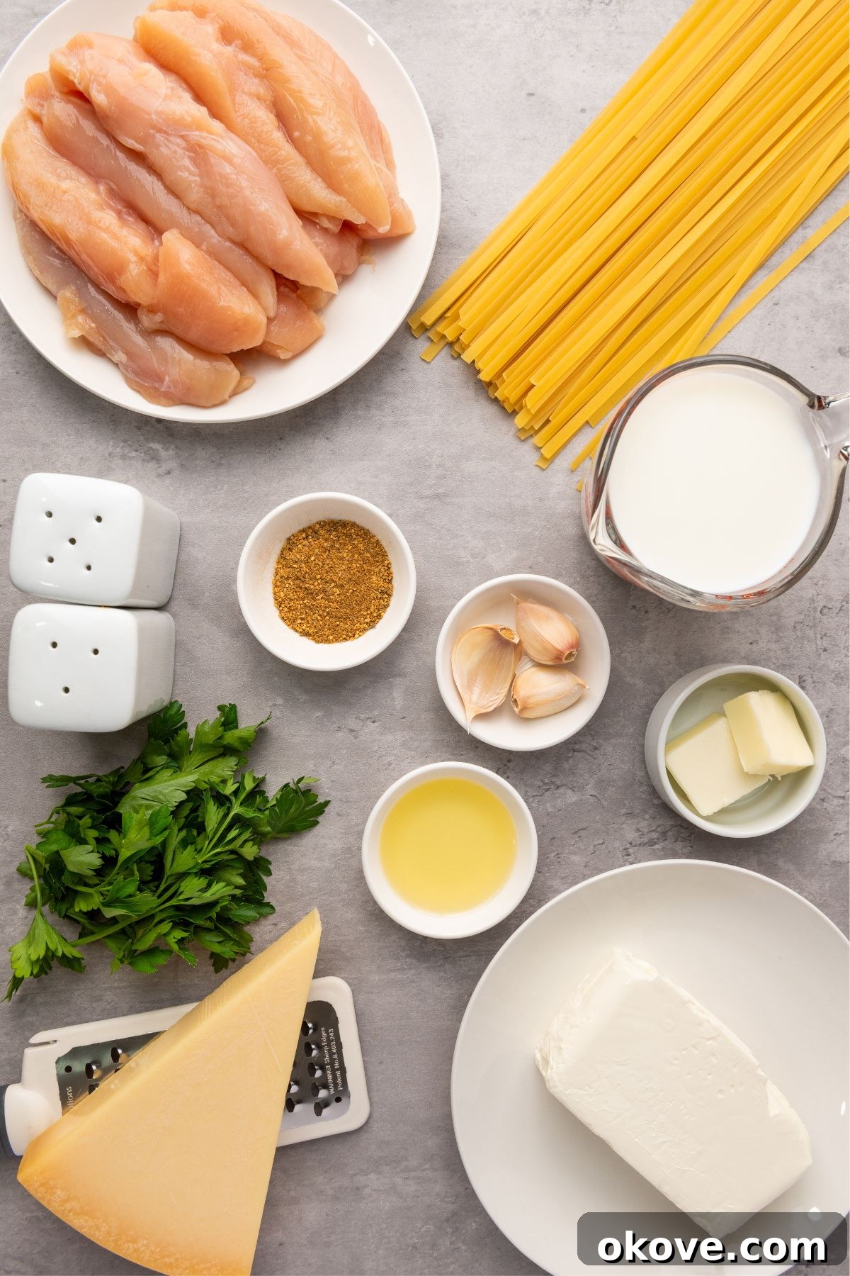 Various ingredients for chicken alfredo, including spices, chicken, and dairy, neatly arranged in small containers on a marble countertop.