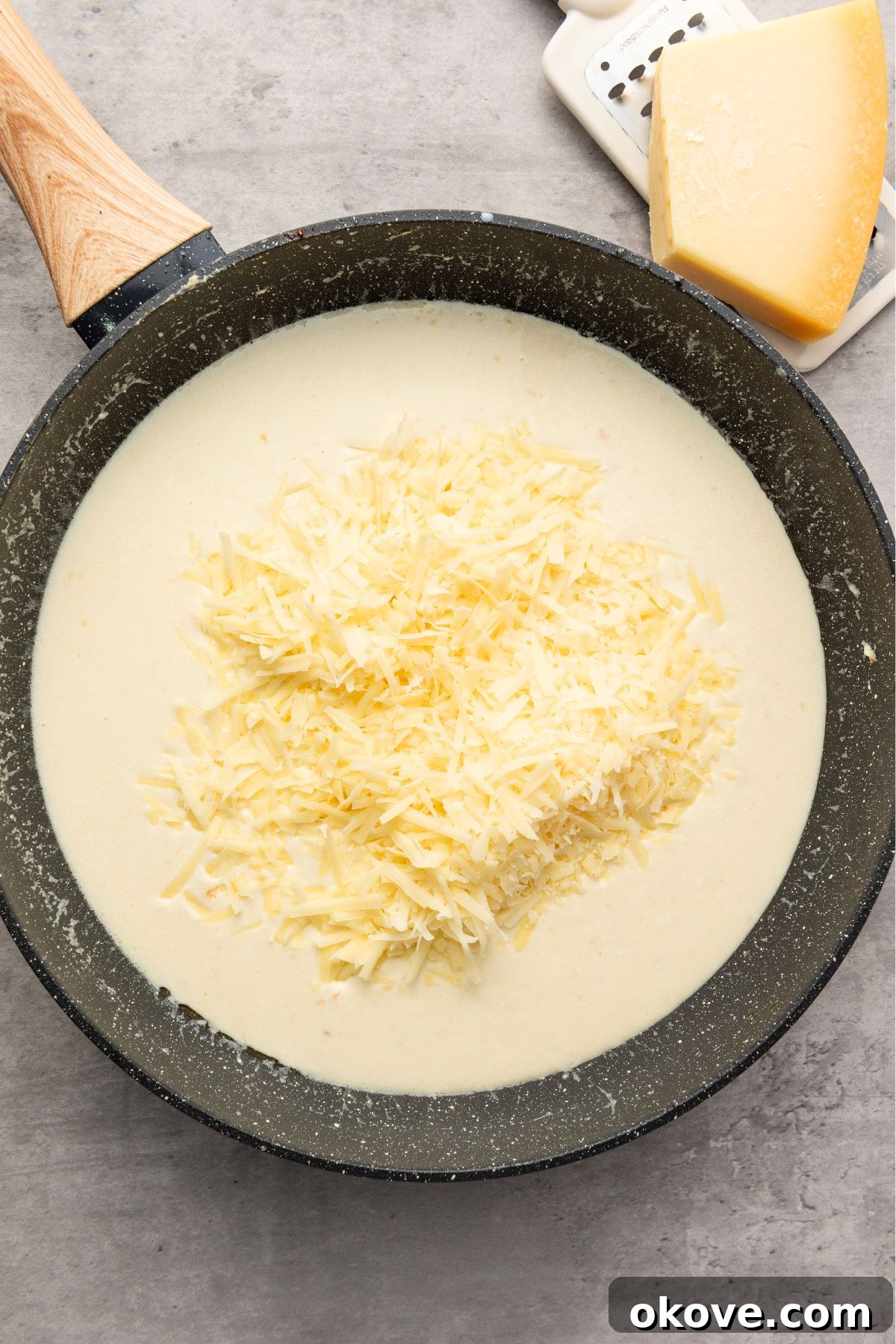 Rich, simmering cream sauce with freshly grated Parmesan cheese being stirred in, creating a smooth texture.