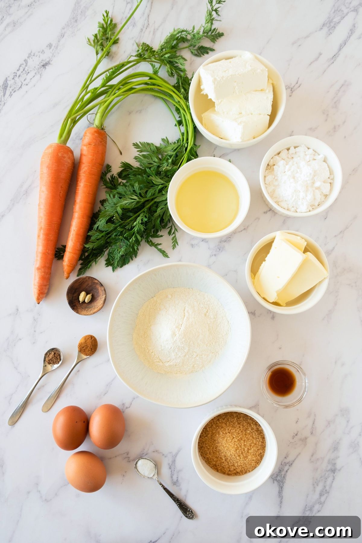 Spiced Carrot Roulade 3 Carrot cake roll ingredients, including flour, sugar, eggs, oil, and spices, neatly arranged in small bowls on a marble countertop.