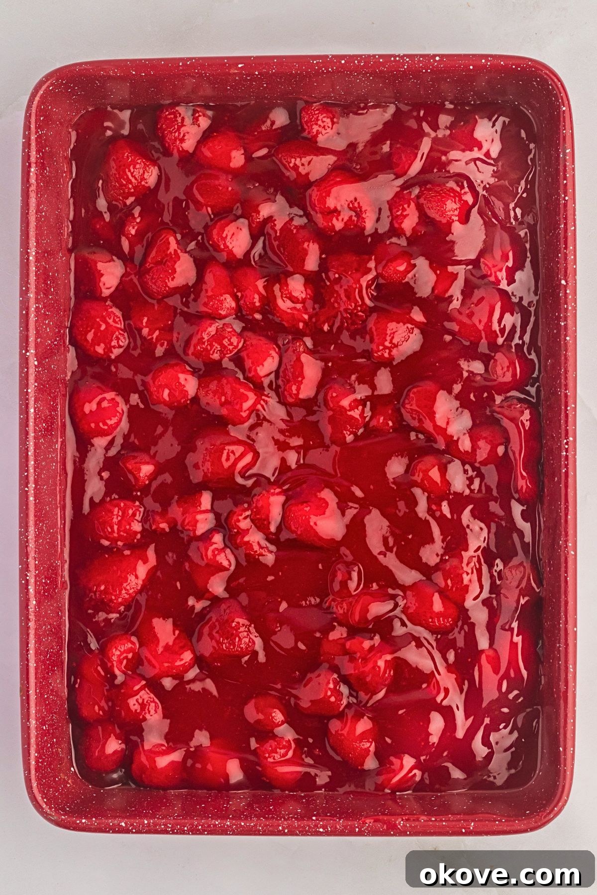 Effortless Strawberry Delight 4 Sweet strawberry pie filling perfectly spread into the bottom of a rectangular cake pan, ready for the next layer.