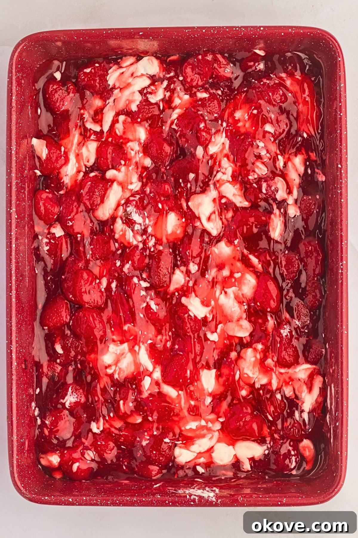 Effortless Strawberry Delight 5 Strawberry pie filling dotted with creamy swirls of cream cheese, creating a delightful pattern in a cake pan.