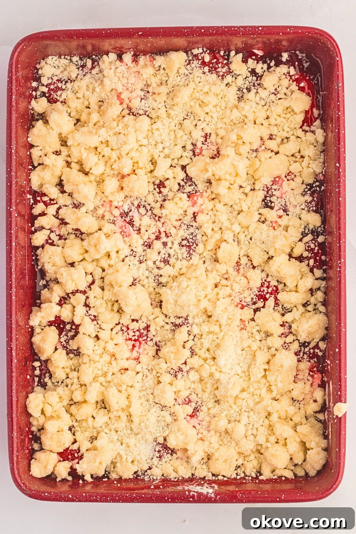 Effortless Strawberry Delight 6 Uncooked buttery cake mix crumble generously dolloped over a vibrant strawberry and cream cheese layer, ready for baking.