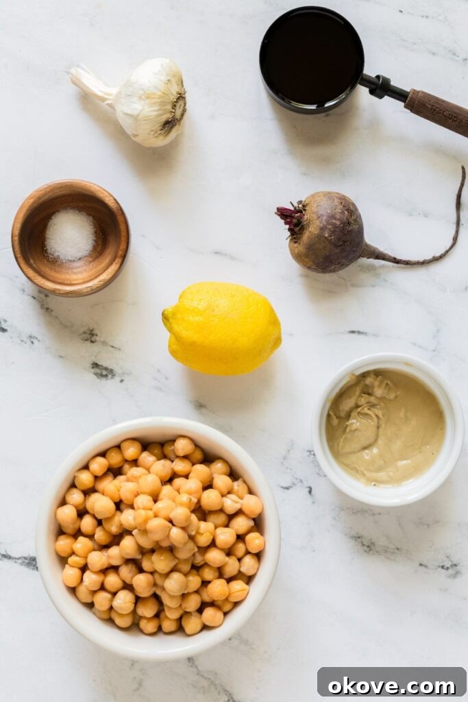 Vibrant Beet Hummus 3 Carefully measured ingredients for beet hummus including a roasted beet, canned chickpeas, extra virgin olive oil, tahini, lemon, garlic cloves, and sea salt, arranged on a marble kitchen counter.