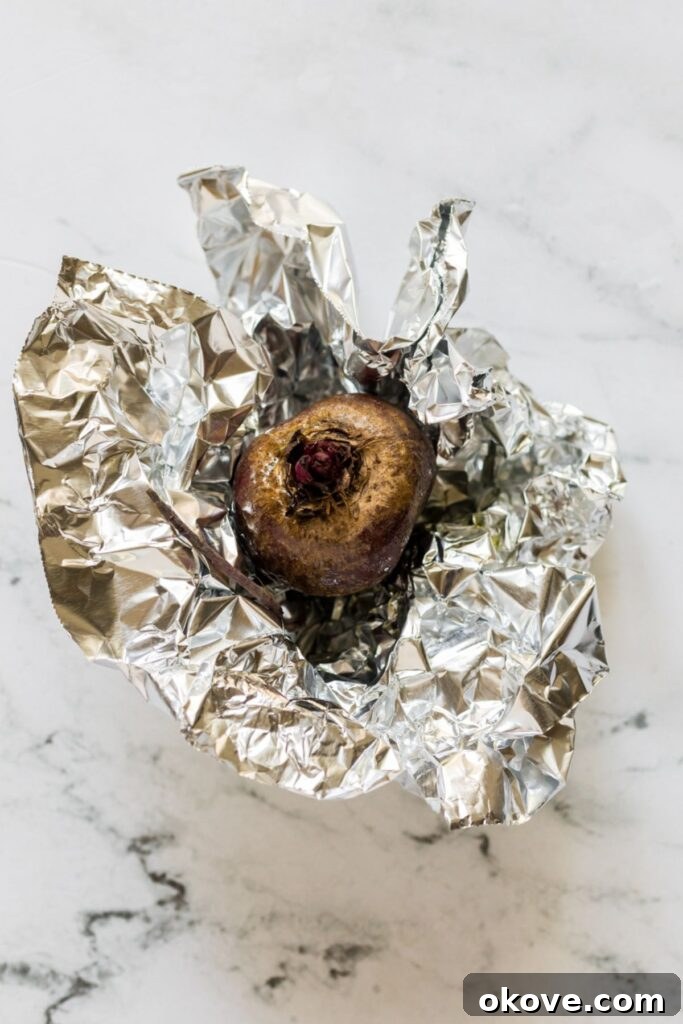 Vibrant Beet Hummus 4 A single small beet, perfectly roasted and still wrapped in aluminum foil, cooling on a marble countertop, ready for peeling and blending into hummus.