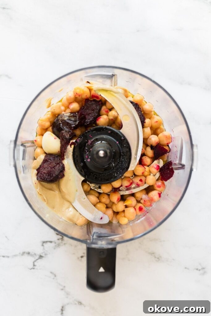 Vibrant Beet Hummus 5 All the key ingredients for beet hummus – roasted beet, drained chickpeas, olive oil, tahini, lemon juice, garlic cloves, and salt – meticulously placed in a food processor bowl, ready for blending into a smooth, vibrant dip.