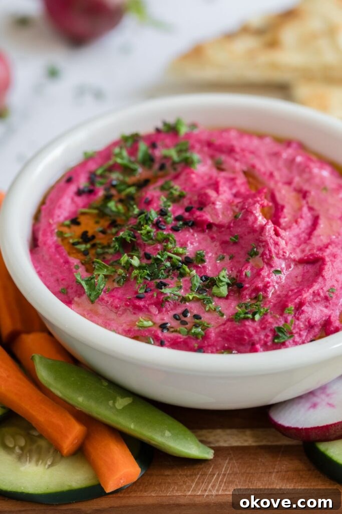 Vibrant Beet Hummus 7 A close-up of a bowl of bright pink beet hummus, garnished with fresh herbs and a drizzle of olive oil, surrounded by an array of colorful vegetables like celery, cucumber, and carrots, perfect for dipping.