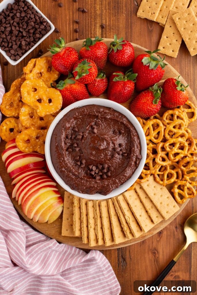 Decadent Chocolate Hummus 7 A pristine white bowl filled with chocolate hummus, surrounded by an appetizing selection of fresh strawberries, pretzels, and apple slices, perfect for dipping.
