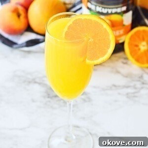 Peach mimosa with an orange slice for garnish on a white marble table.