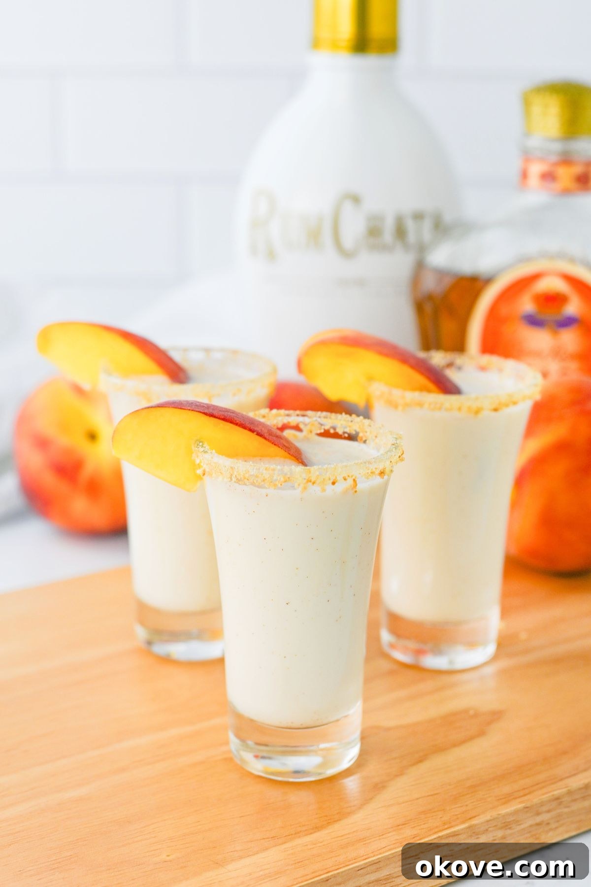 Small shot glass with creamy peach cobbler shot, garnished with a fresh peach slice, invitingly presented.
