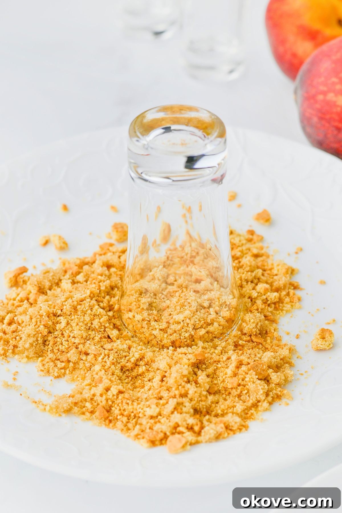 A shot glass being carefully dipped into a mixture of graham cracker crumbs, brown sugar, and cinnamon to create a perfectly coated rim.