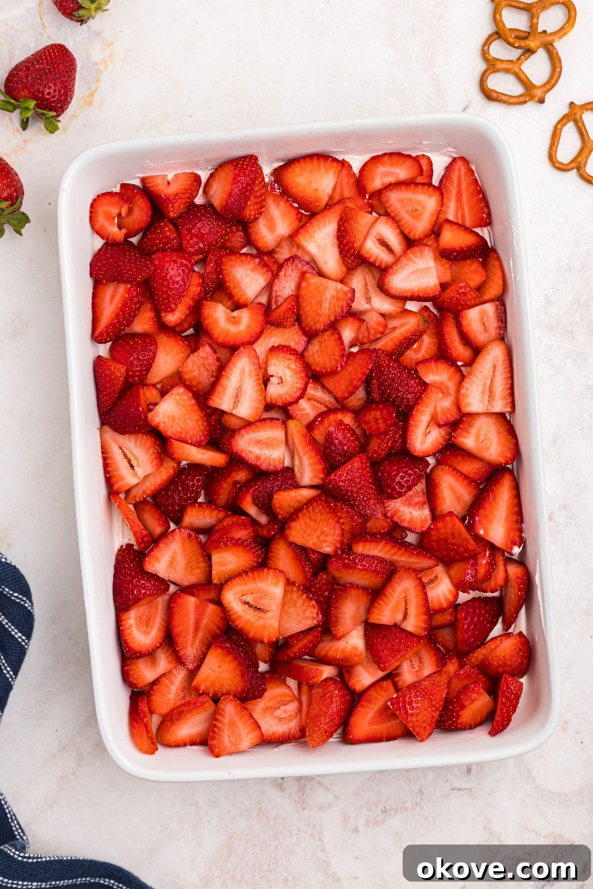 Strawberry Pretzel Dream 11 Strawberry slices spread over whipped topping in white baking dish.