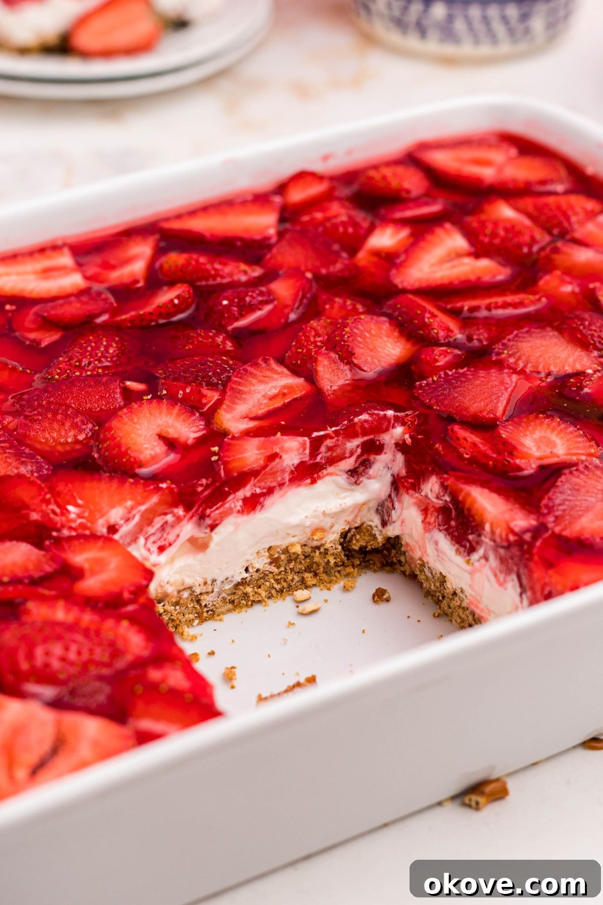 Strawberry Pretzel Dream 14 Layers of pretzel crust, whipped filling, and strawberries in J-ello, in a white baking dish with a slice missing.