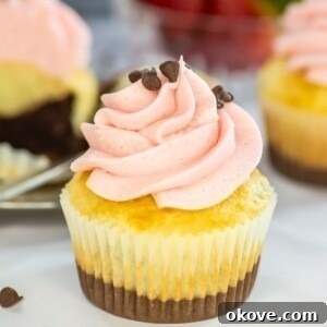 Neapolitan cupcakes with swirling pink frosting on top, in front of a bowl of fresh strawberries.