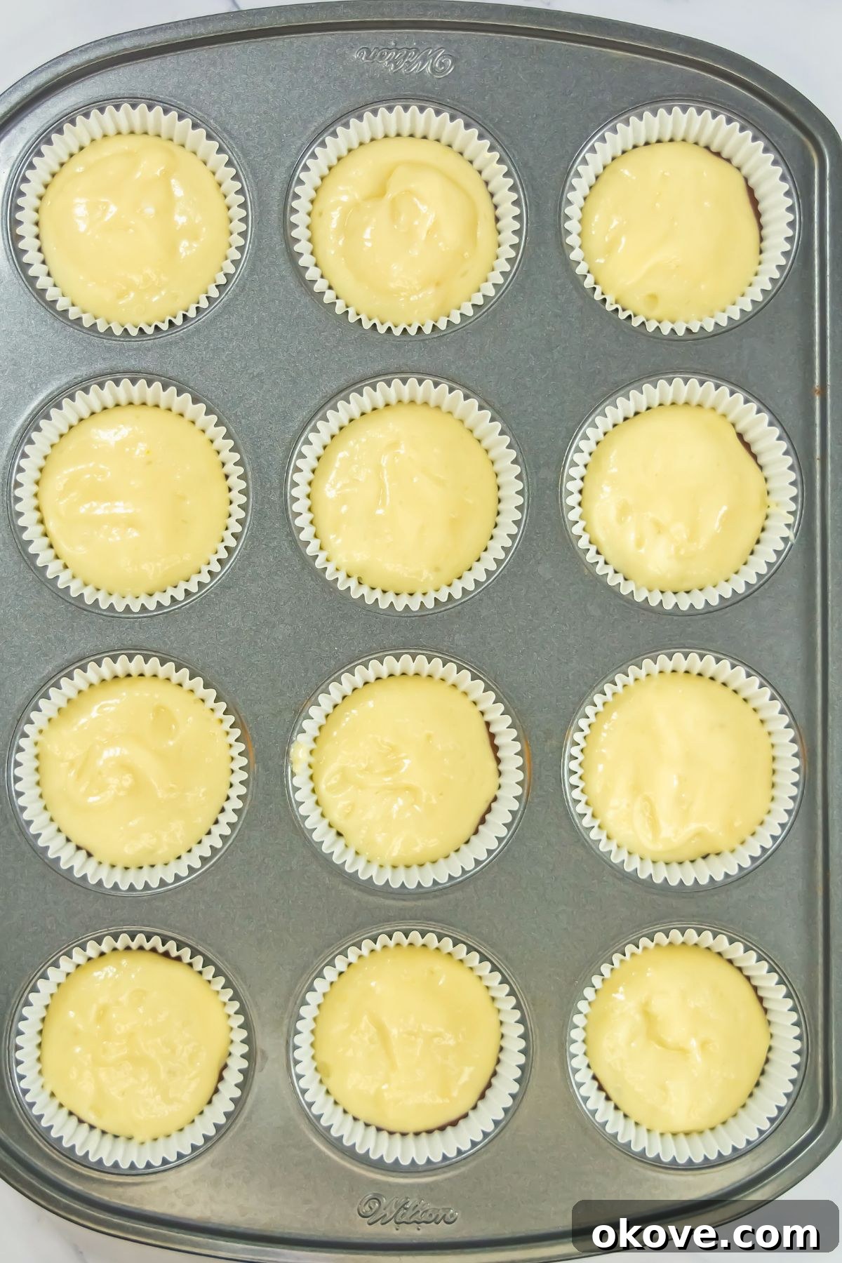 Neapolitan Swirl Cupcakes 5 Light vanilla cake batter is carefully spooned over a dark chocolate cake batter base, meticulously placed into individual cupcake liners within a baking pan, creating distinct layers.