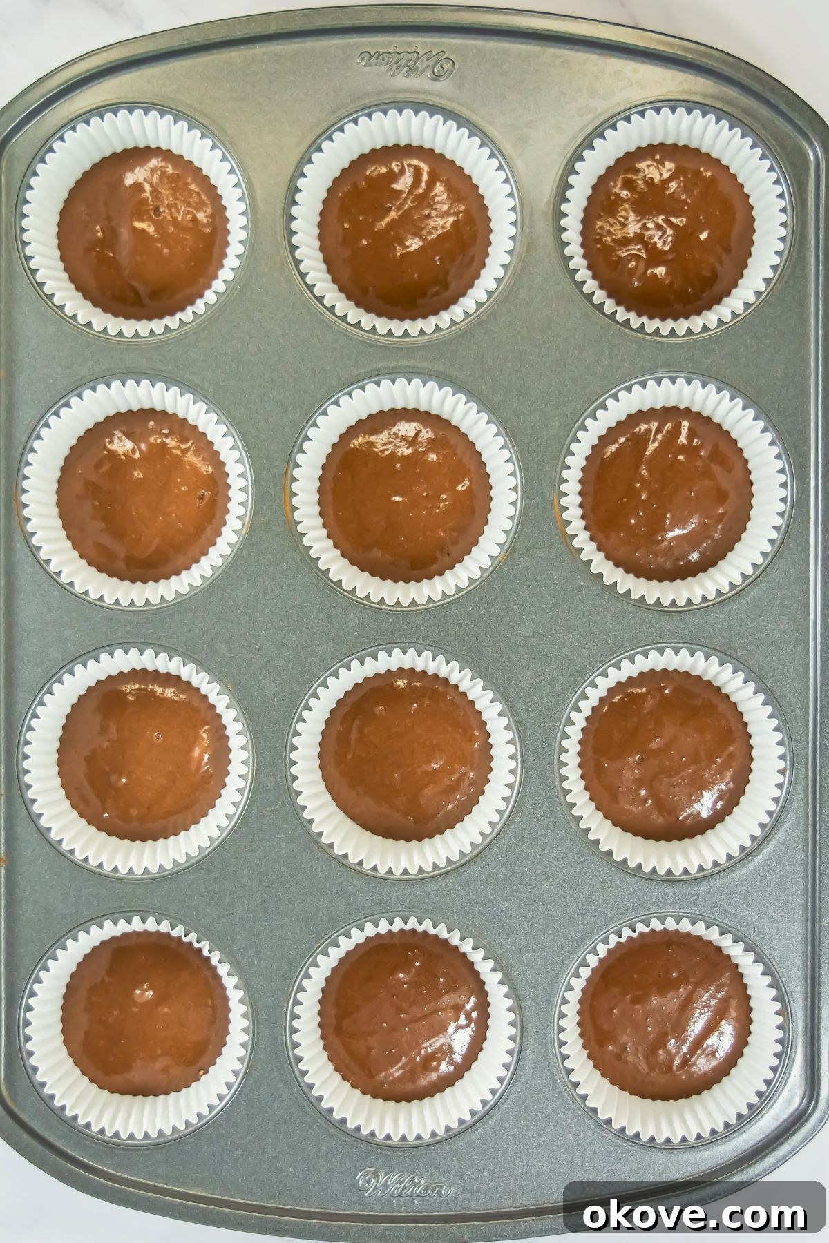 Neapolitan Swirl Cupcakes 6 The chocolate cake batter is neatly settled into individual cupcake liners, arranged in a baking pan, creating the foundational layer before the vanilla batter is added and before baking.