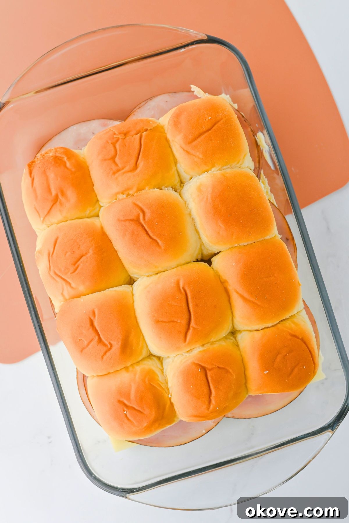 Assembled ham and cheese sliders layered in a glass baking dish, ready for the butter topping.