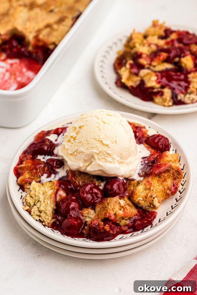 Golden crusted cherry dump cake on white plates topped with vanilla ice cream.