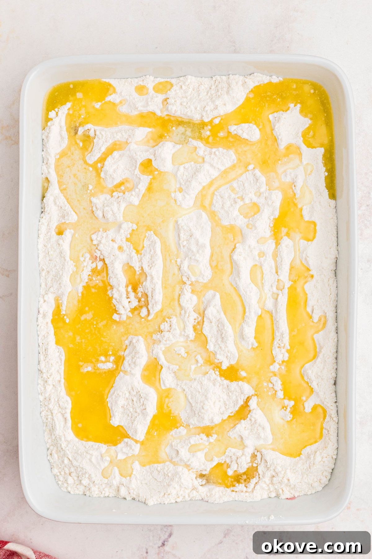 Cherries topped with yellow cake mix powder, topped with melted butter in a white casserole dish before being baked.