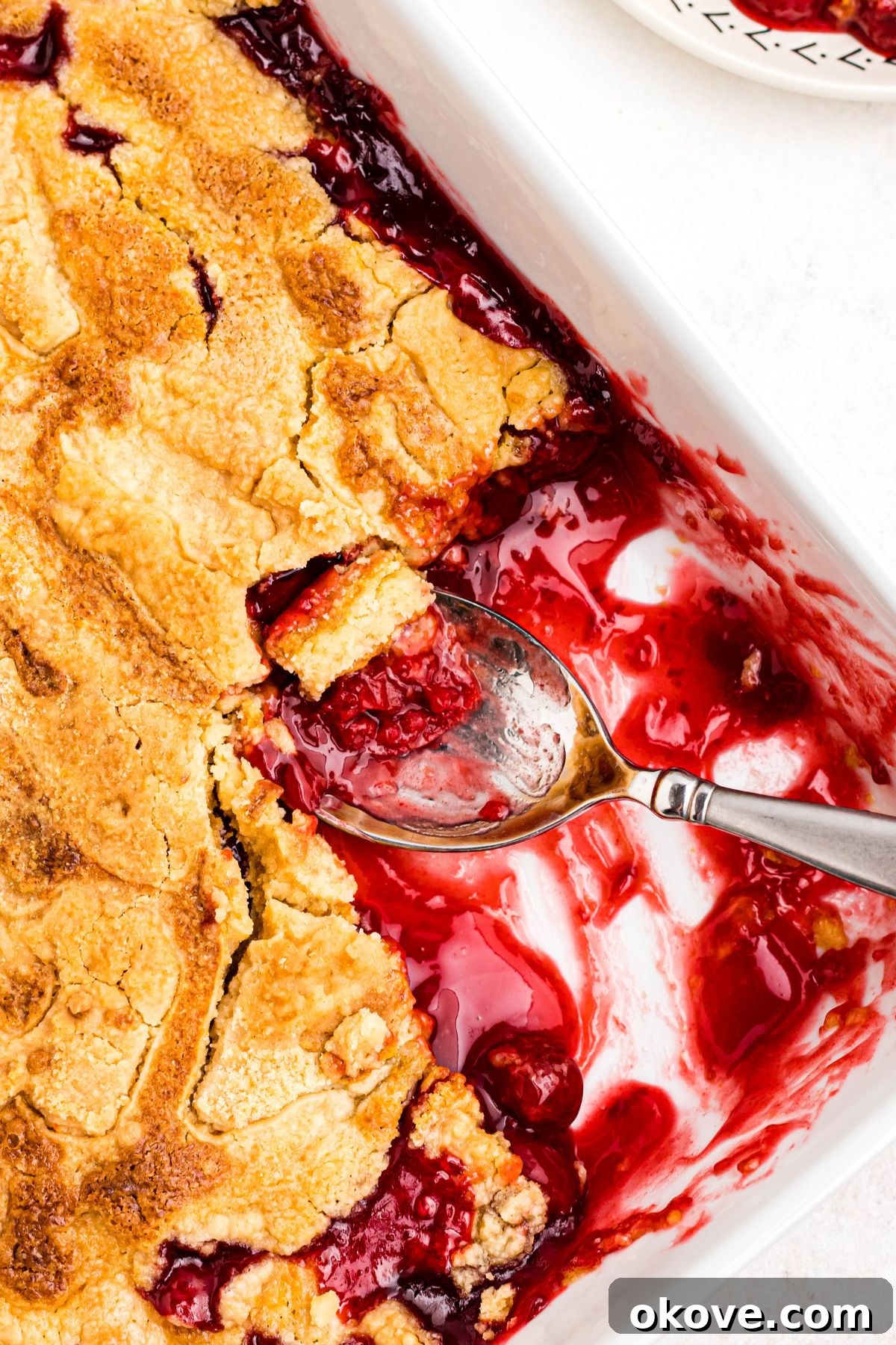 Cherry dump cake baked until golden brown with a piece missing and a spoon in the corner.