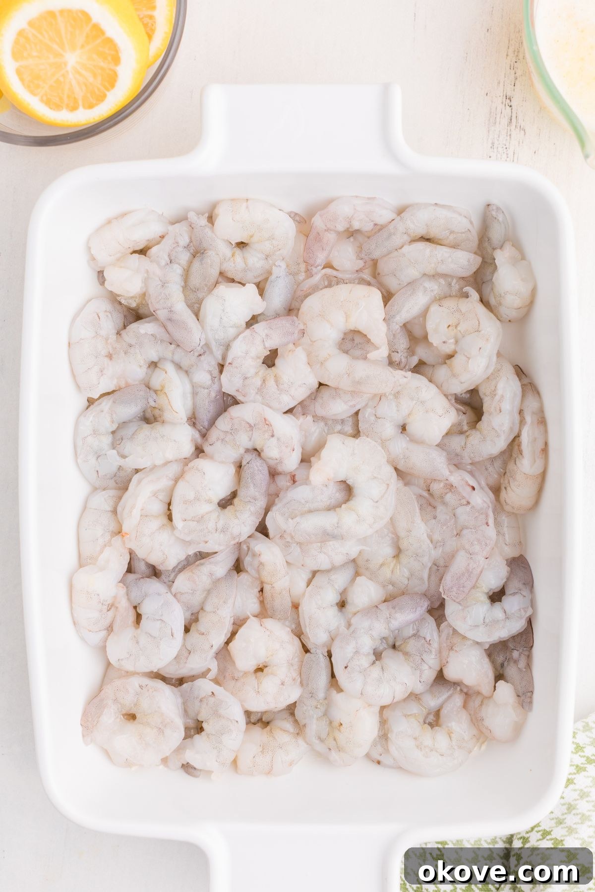 Uncooked, raw shrimp laid out in a perfect single layer within a white baking dish, ready for seasoning and baking.