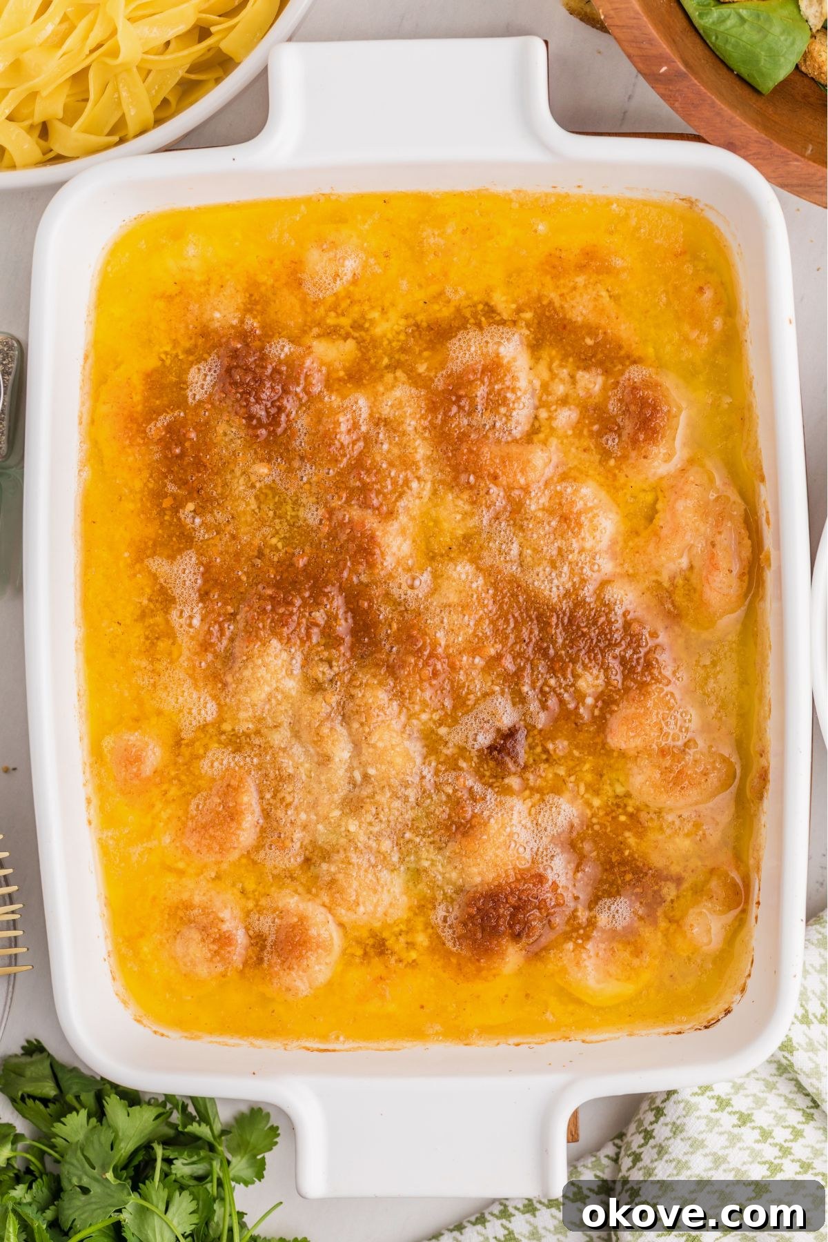 A baked, cheesy shrimp scampi dish, golden brown and bubbling, fresh from the oven in a pristine white baking dish.