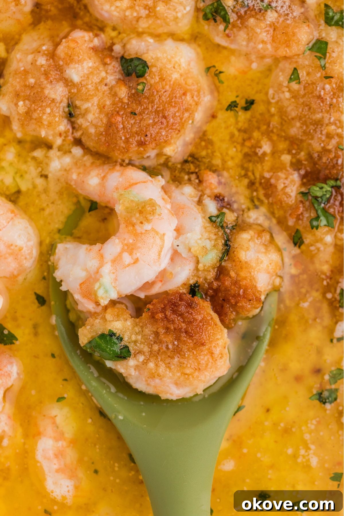 A serving spoon gracefully scoops a generous portion of cheesy, buttery baked shrimp scampi from the baking dish, revealing the succulent shrimp beneath.