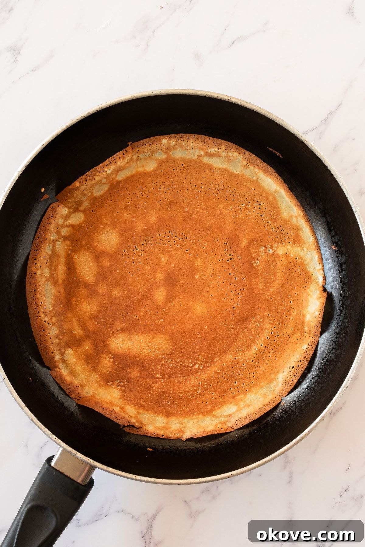 Stacked Crepe Dream 4 Very thin crepes being expertly made in a black nonstick skillet, cooked until they achieve a delicate golden-brown color around the edges.