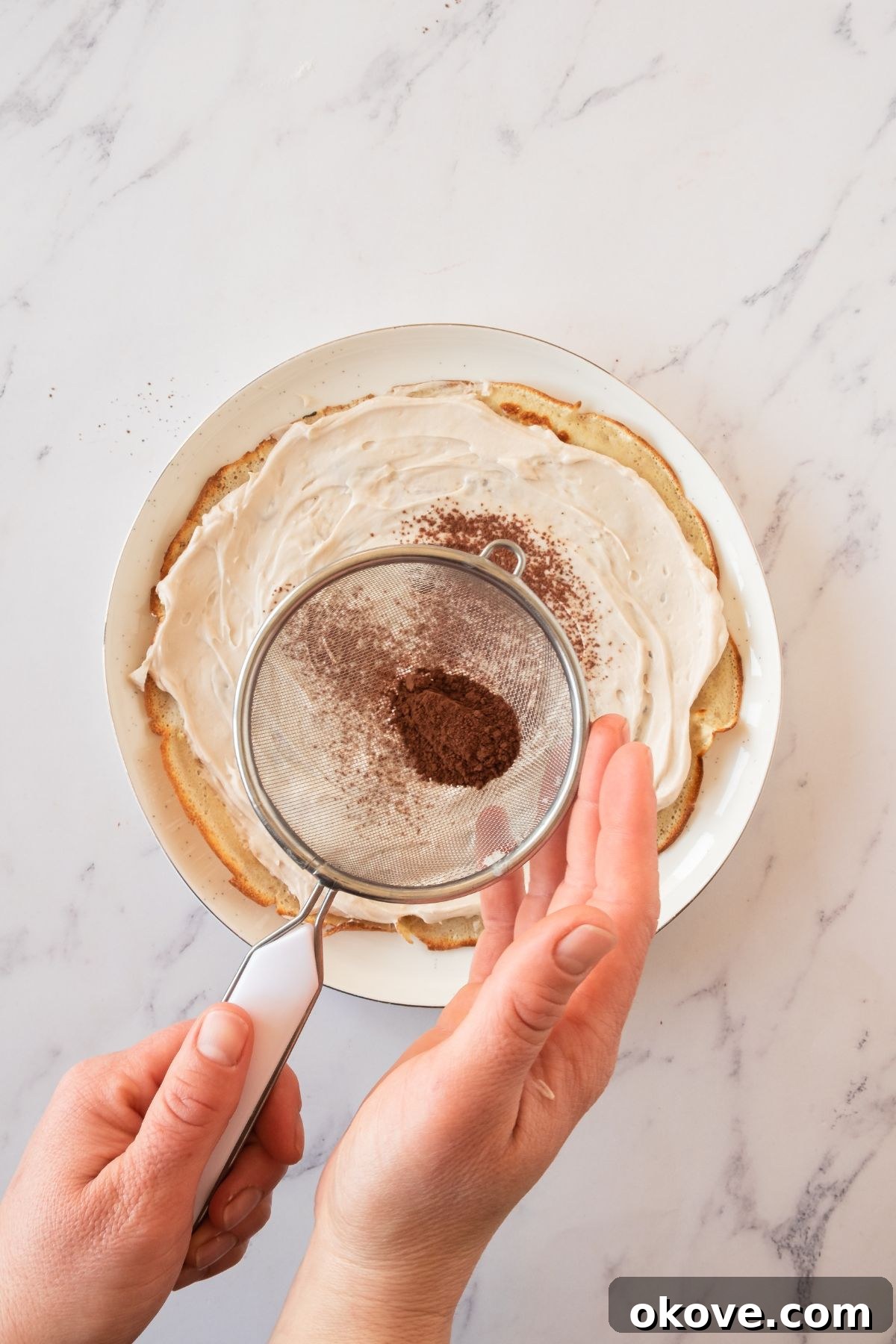 Stacked Crepe Dream 6 Detailed shot of the crepe cake assembly process, showing layers of thin crepes generously topped with creamy mascarpone frosting, then lightly dusted with fine cocoa powder.