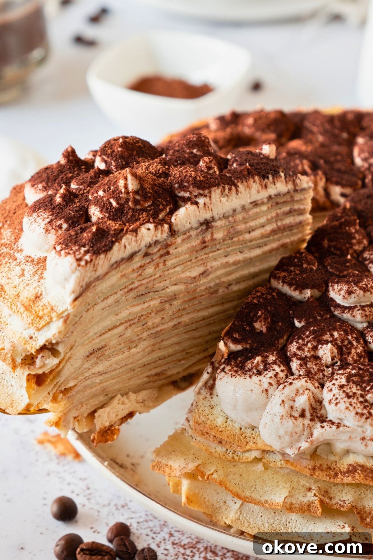 Stacked Crepe Dream 8 A beautifully layered slice of tiramisu crepe cake being carefully lifted off a cake plate, prominently displaying its delicate, alternating layers of crepe and creamy filling.