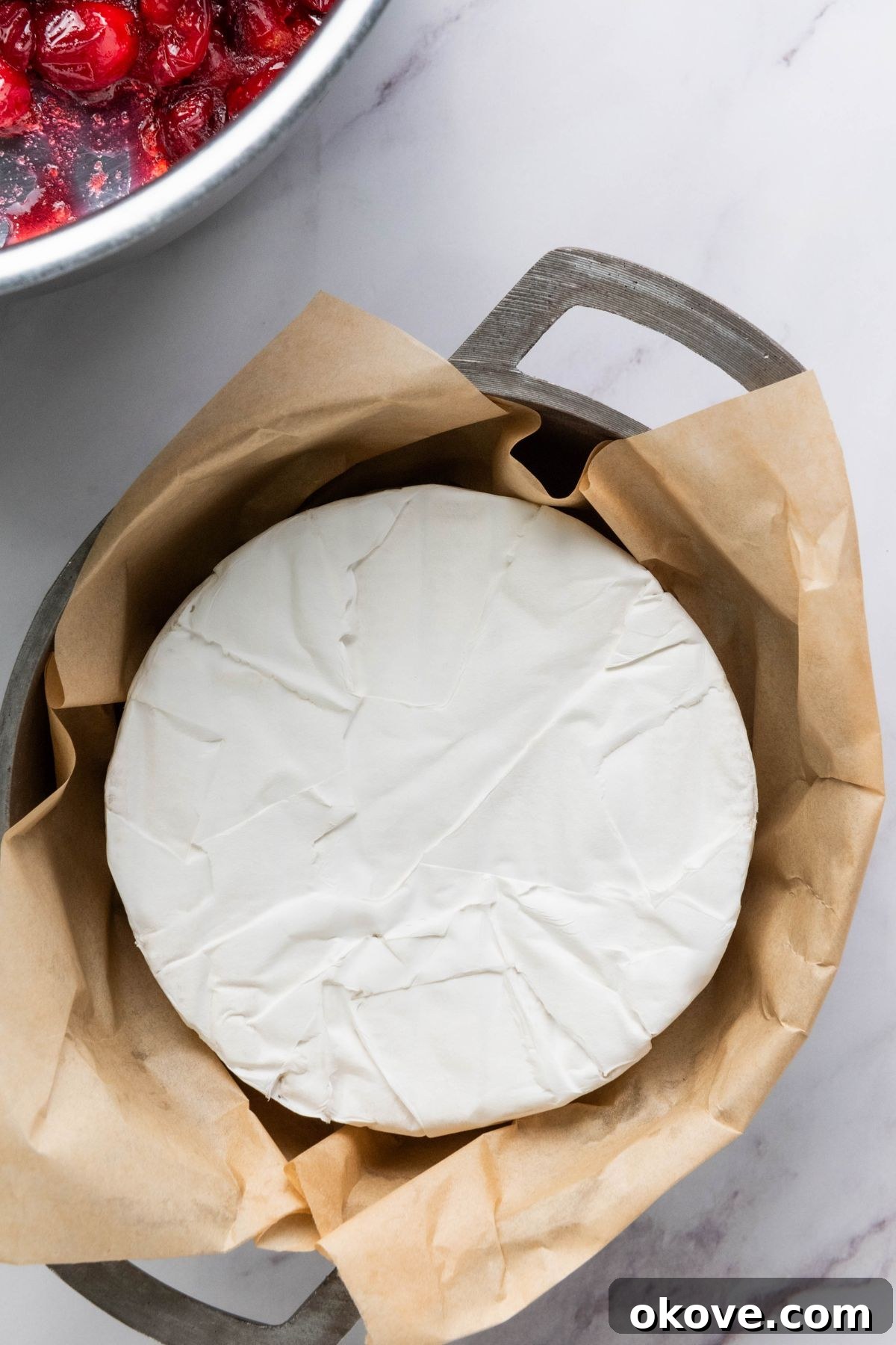 Warm Brie Delight 4 A pristine wheel of brie cheese, carefully placed in a small, round oven-safe baking dish, ready for its delicious toppings and baking process.