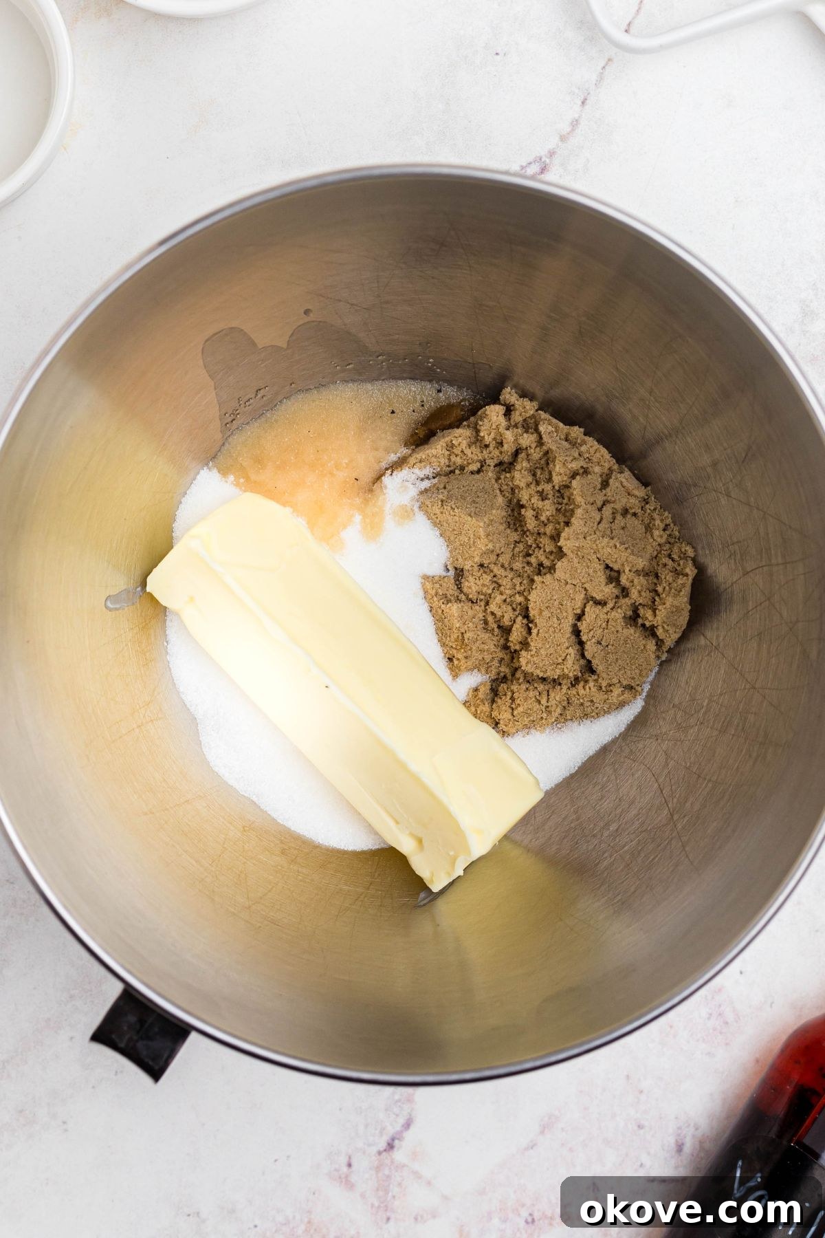 Softened unsalted butter, granulated sugar, and light brown sugar being expertly creamed together in a gleaming silver mixing bowl using an electric mixer, creating a light and airy mixture.