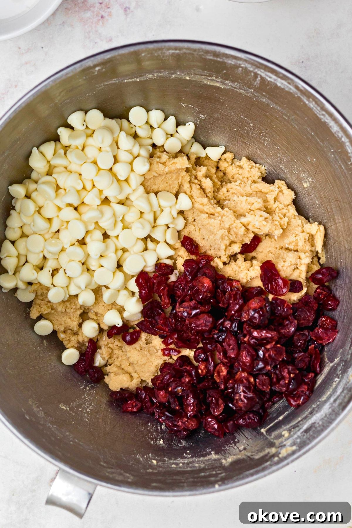 Vibrant dried cranberries and creamy white chocolate chips being gently folded into the freshly made cookie dough in a large silver bowl, ensuring even distribution.
