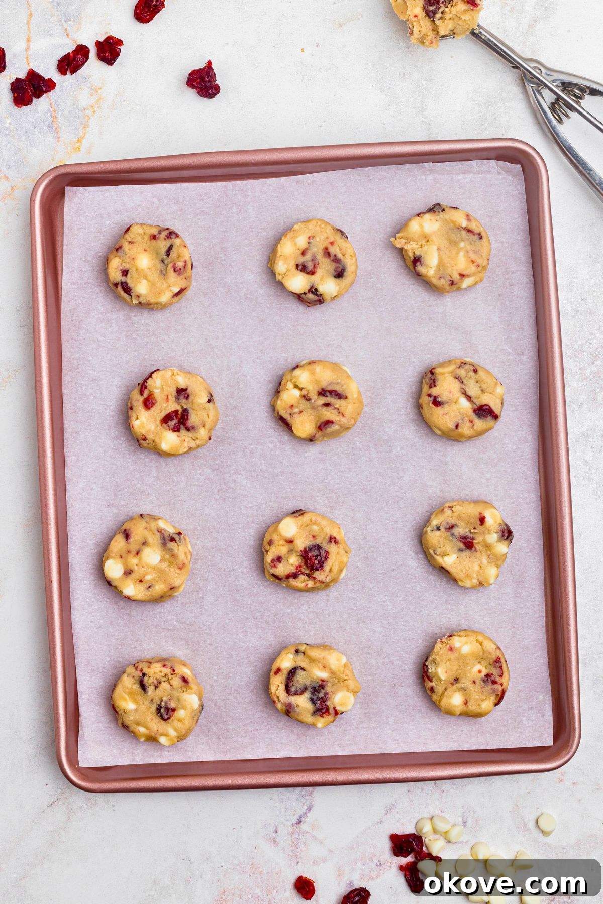 Uniform balls of white chocolate cranberry cookie dough, adorned with visible cranberries and chips, carefully spaced on a prepared baking sheet, ready for the oven.