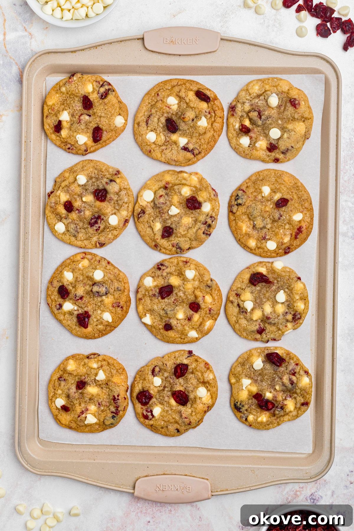 A batch of freshly baked white chocolate cranberry cookies, with golden edges and soft centers, resting on a baking sheet lined with parchment paper.