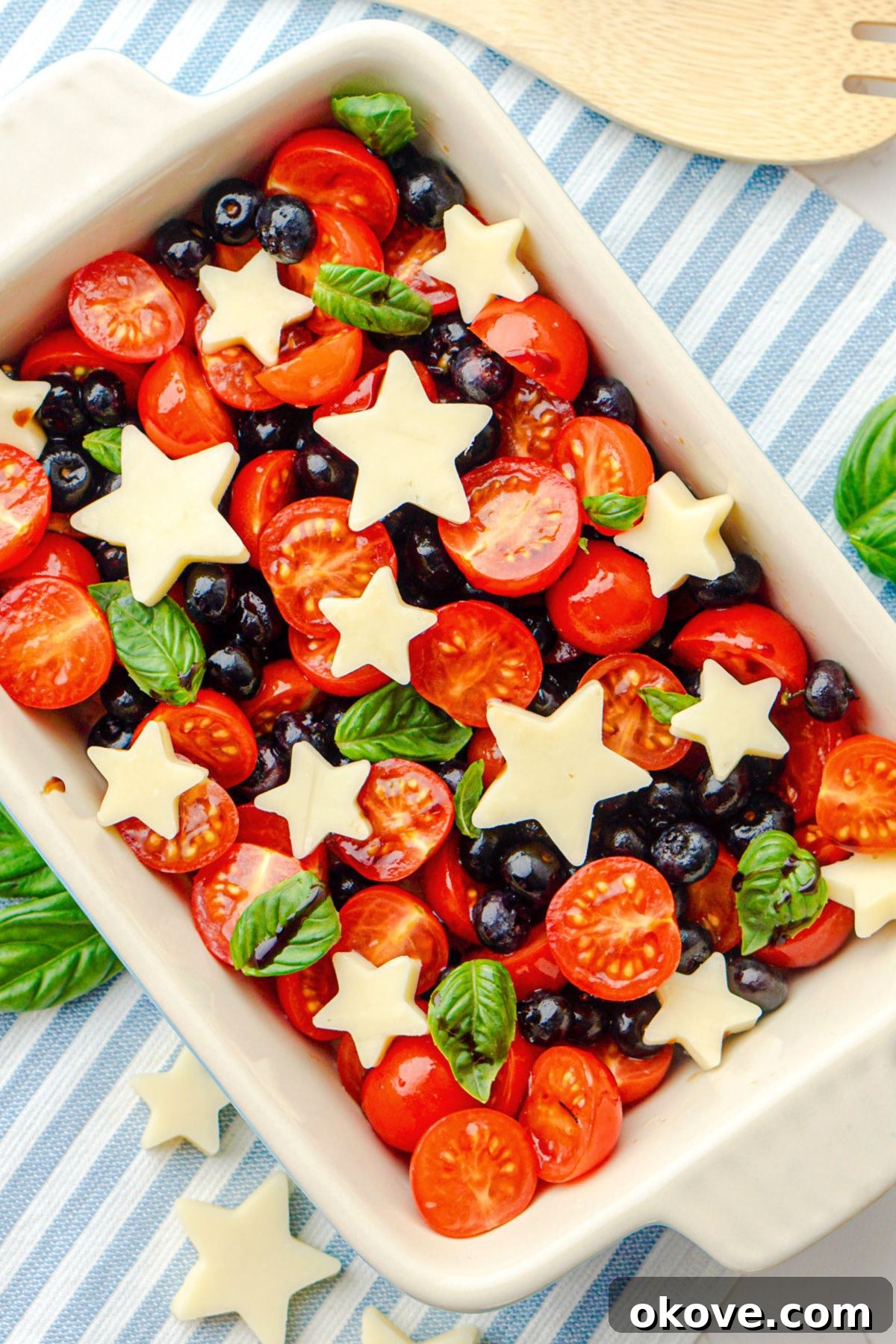 A festive Berry Caprese Salad featuring star-shaped mozzarella, red cherry tomatoes, and blue blueberries, artfully arranged in a rectangular serving dish.