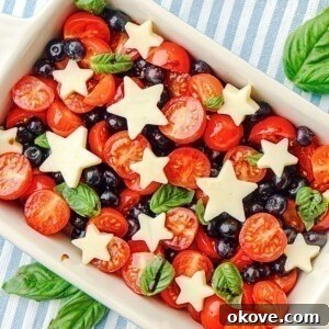 A vibrant Berry Caprese Salad with star-shaped mozzarella, blueberries, and cherry tomatoes in a rectangular serving dish.