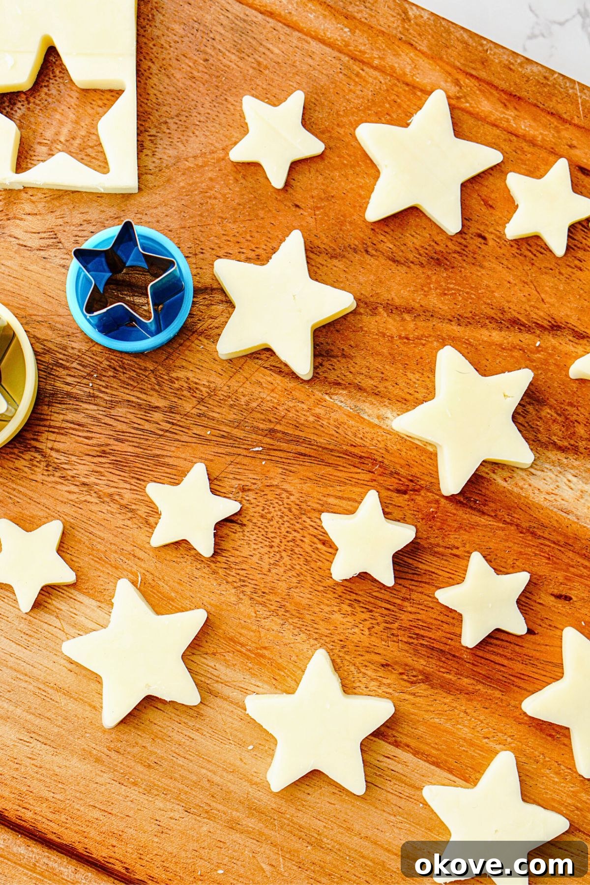 A block of fresh mozzarella cheese being cut into star shapes using a small star-shaped cookie cutter on a wooden cutting board.
