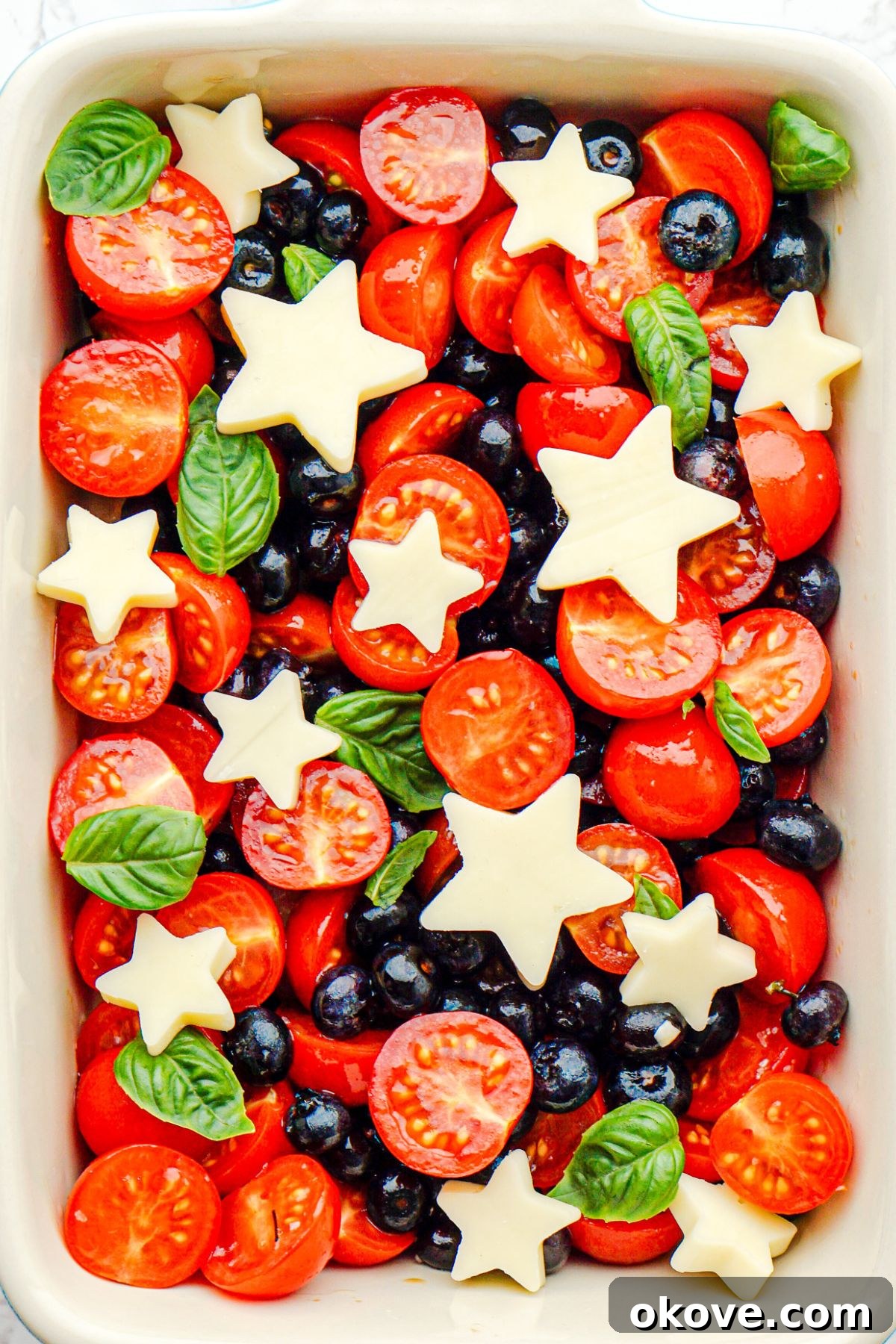 The final Berry Caprese Salad presented in a rectangular baking dish, showcasing the beautiful arrangement of star-shaped mozzarella, red tomatoes, and blue blueberries, ready to be served.