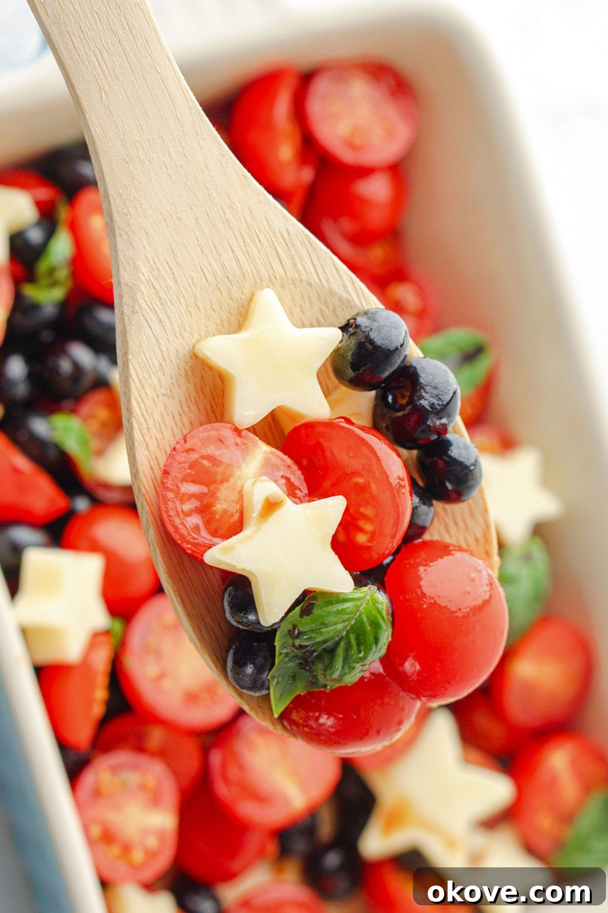 A wooden spoon delicately holding a scoop of Berry Caprese Salad, featuring visible star mozzarella, sweet blueberries, and juicy tomatoes, highlighting the fresh and appealing textures.