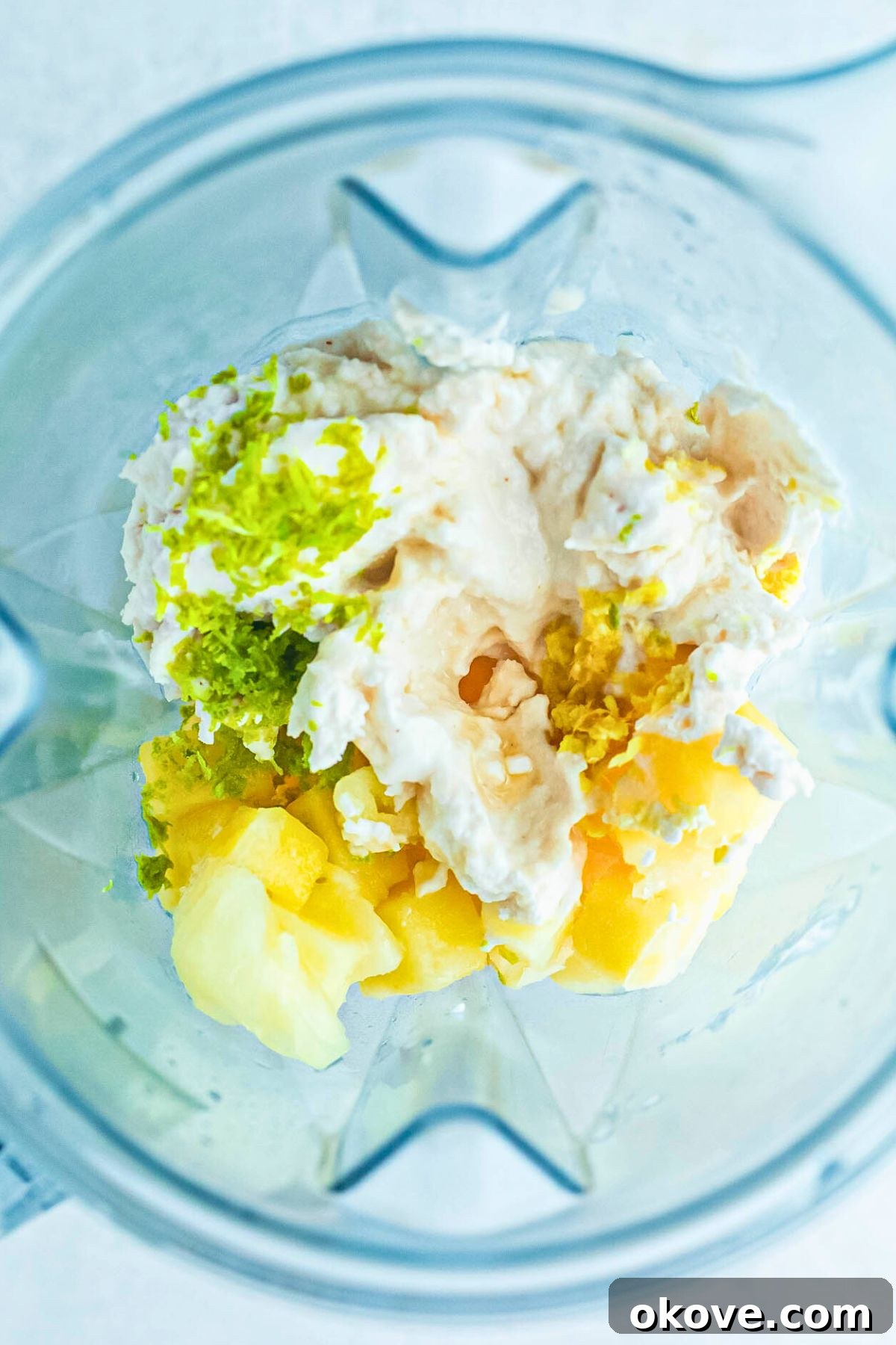 Ingredients for virgin pina colada, including frozen pineapple, coconut milk, pineapple juice, lime, ginger, salt, and maple syrup, added to a high-speed blender before mixing.
