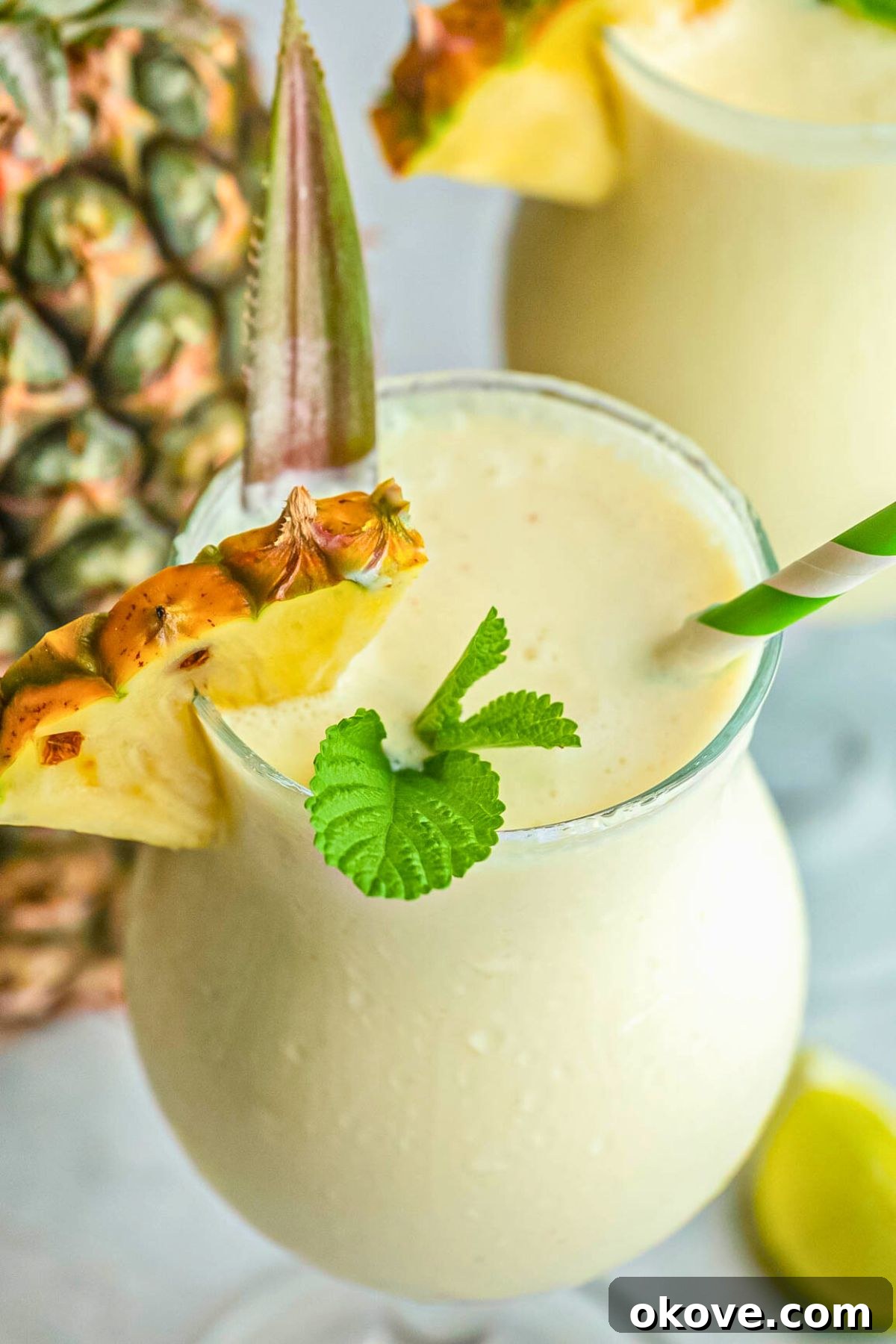 Frozen blended virgin pina colada drink in a frosted glass, garnished with a pineapple wedge and a green straw, ready to be enjoyed.