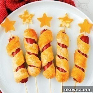 Five hot dogs wrapped in crescent roll dough, baked, and then topped with cheese stars, on a round white plate.