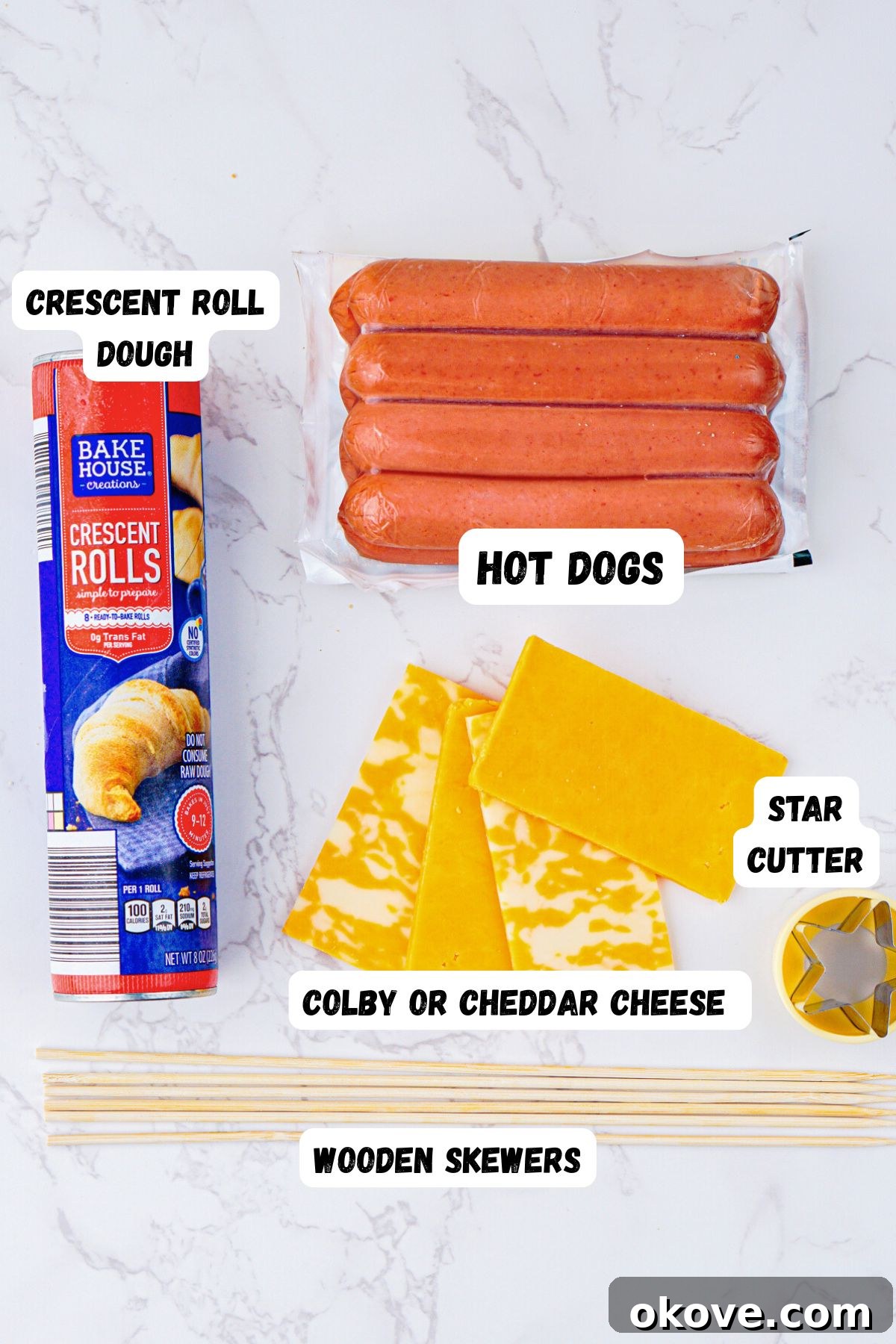 Dough, hot dogs, cheese, and a star shaped cutter on a white marble table.