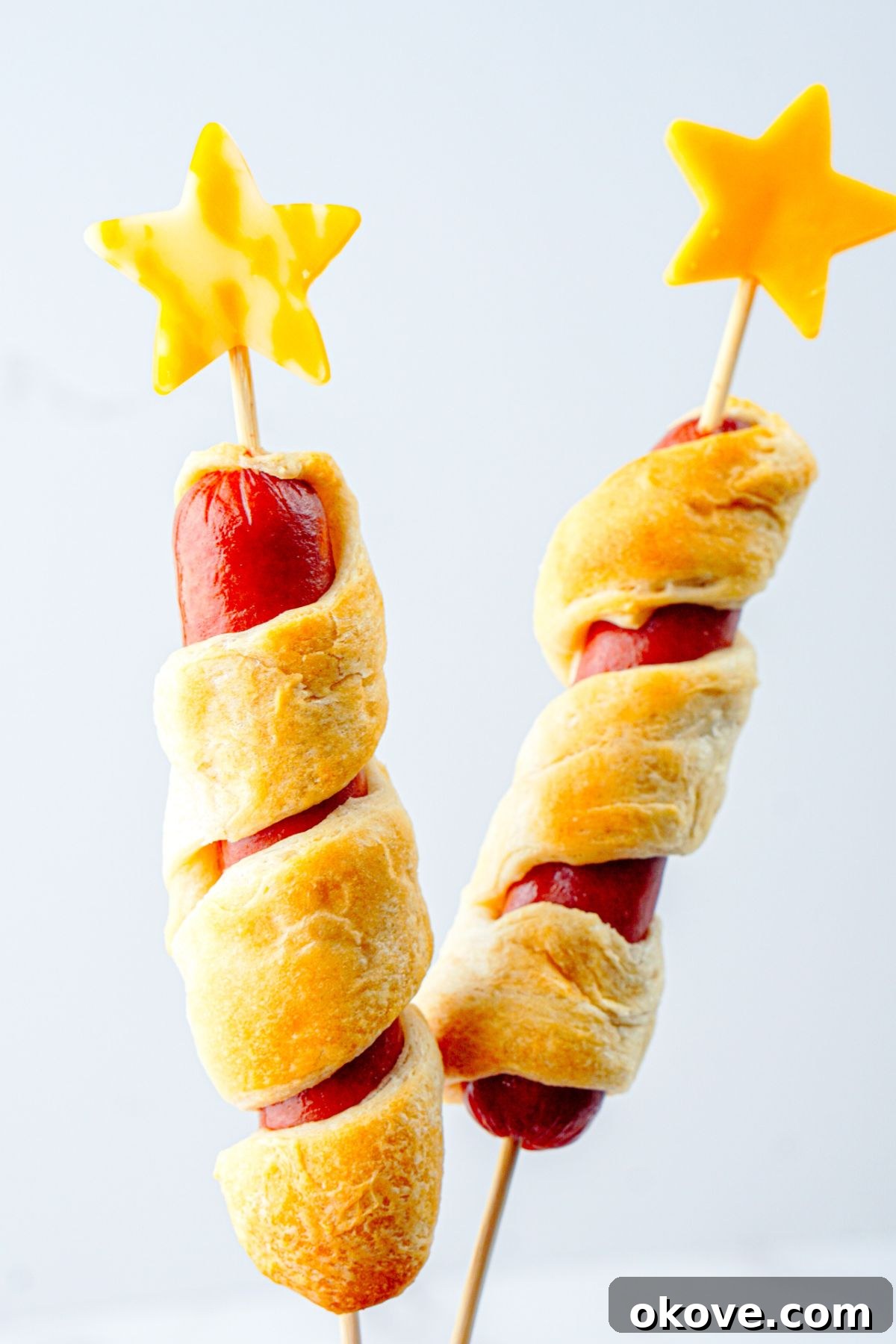 Baked hot dogs with cheese stars being placed on top of them onto a skewer.