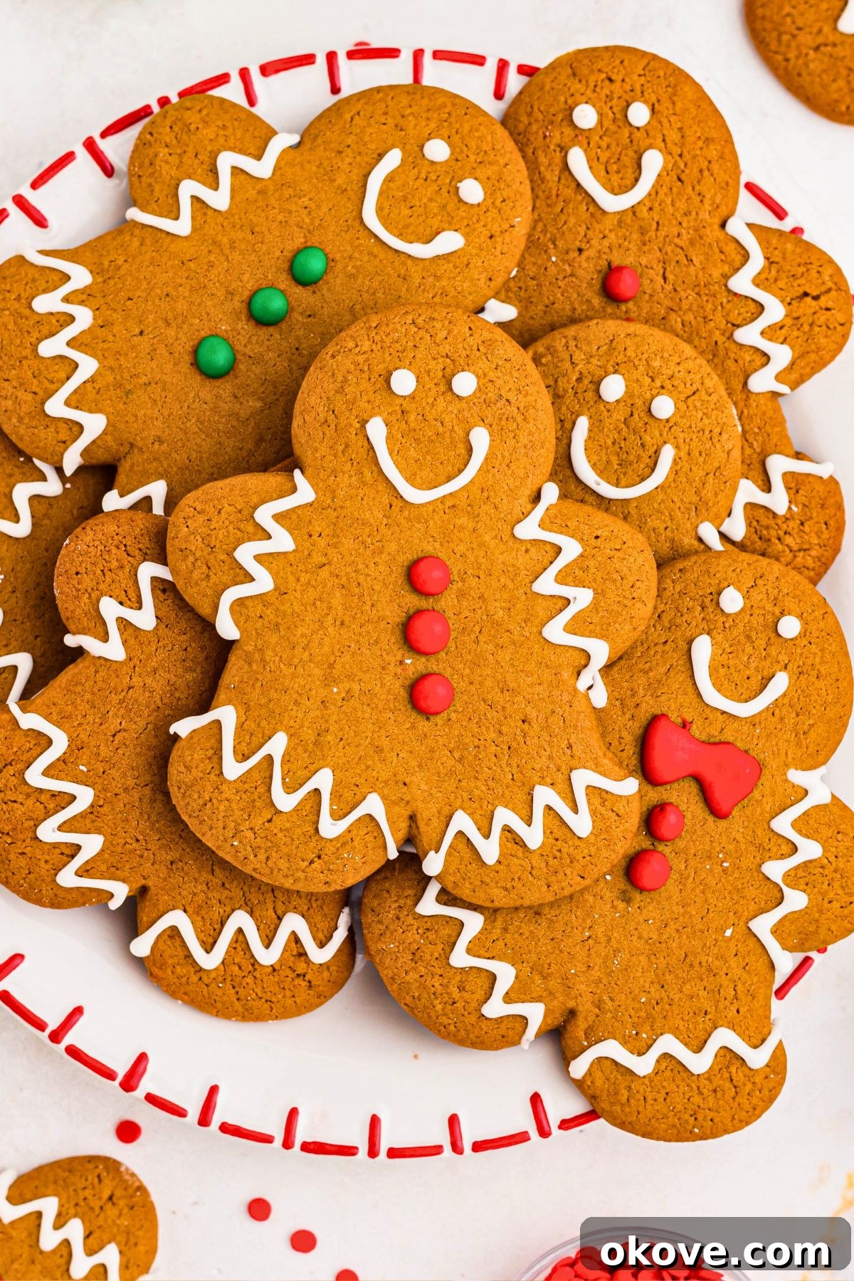 Festive Gingerbread Delights 11 Gingerbread cookies stacked on a white plate with sprinkles and other cookies scattered around the plate.